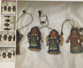 Three small figurines hanging from strings on a textured surface.