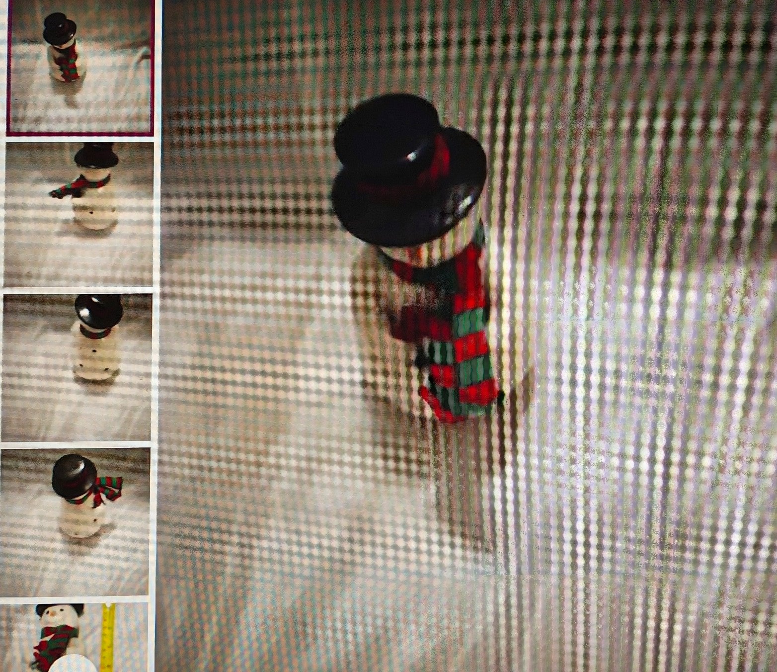 Small snowman figurine with a black top hat and plaid scarf on a textured surface.