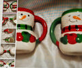 Snowman-themed mugs with red and green accents on a checkered fabric background.