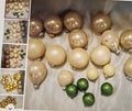 Collection of gold, beige, and green Christmas ornaments on a light surface.