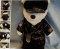 Stuffed bear in military uniform with an American flag patch and dog tag, on a textured gray background.
