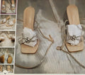 Beige sandals with decorative chain and bow on a textured surface