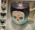 Black and blue mug with colorful skull design on a reflective surface