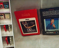 Red RCA cassette tape with a display of other cassette tapes on a gray surface.