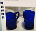 Two cobalt blue glass mugs on a reflective surface with a blurred background
