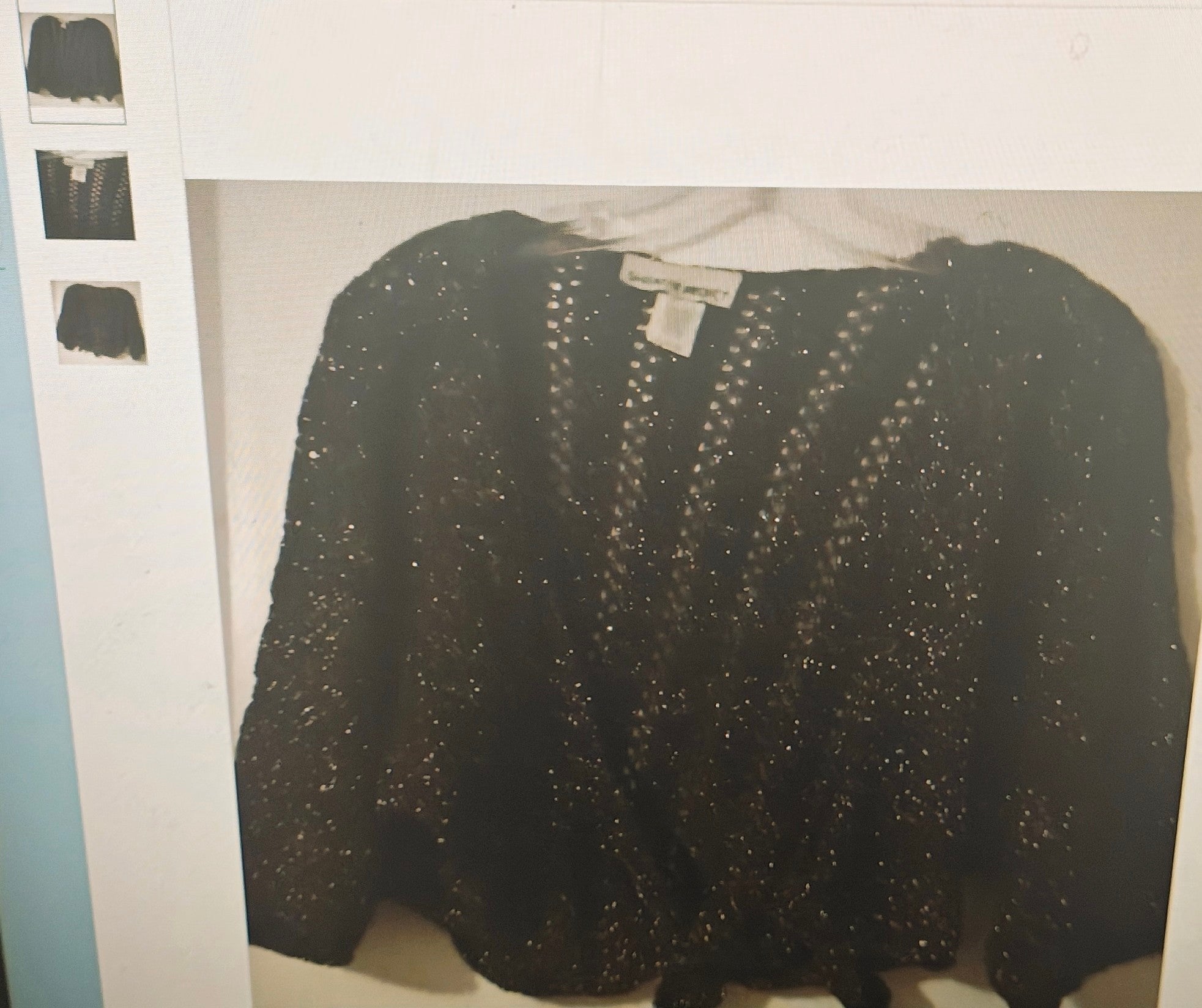 Black sequined top on a hanger against a white background