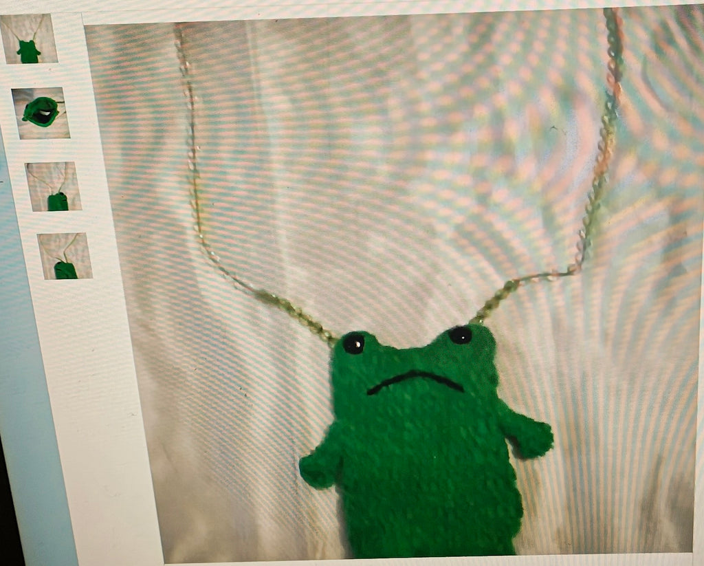 Green plush frog toy with a sad expression on a textured surface