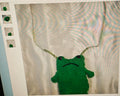 Green plush frog toy with a sad expression on a textured surface