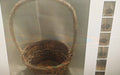 A woven wicker basket with a tall loop handle, shown against a gray background with a narrow vertical strip of smaller inset images on the right.