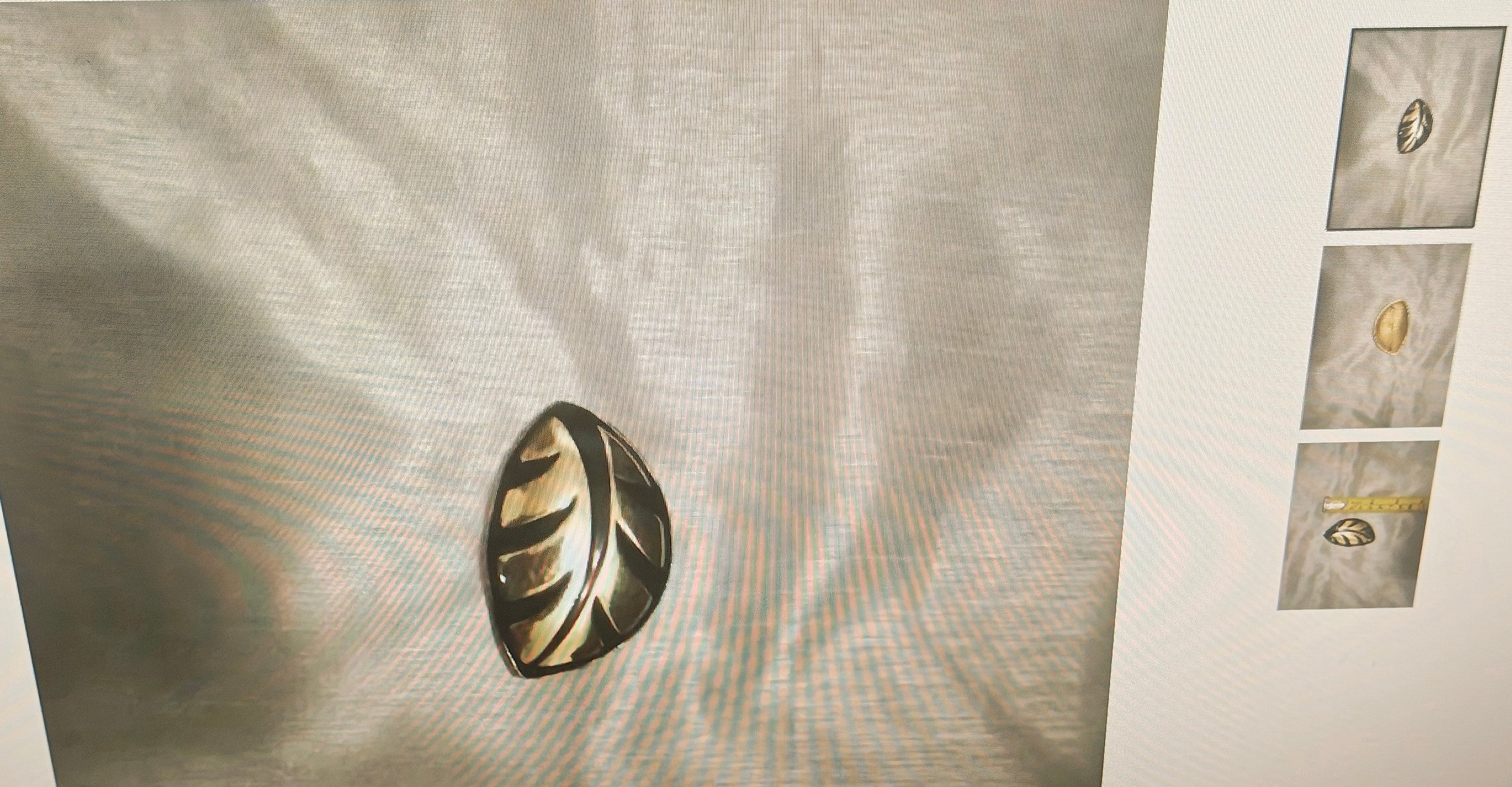 A metallic oval pin with a leaf-like cutout pattern in a gold and silver-tone finish, displayed on a textured light gray fabric background with three smaller thumbnail views on the right.
