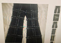 Black denim jeans with a distinctive grid pattern made from frayed, textured rope or cord overlays, shown on a light-colored surface.