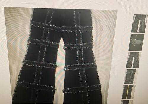 Black denim jeans with a distinctive grid pattern made from frayed, textured rope or cord overlays, shown on a light-colored surface.